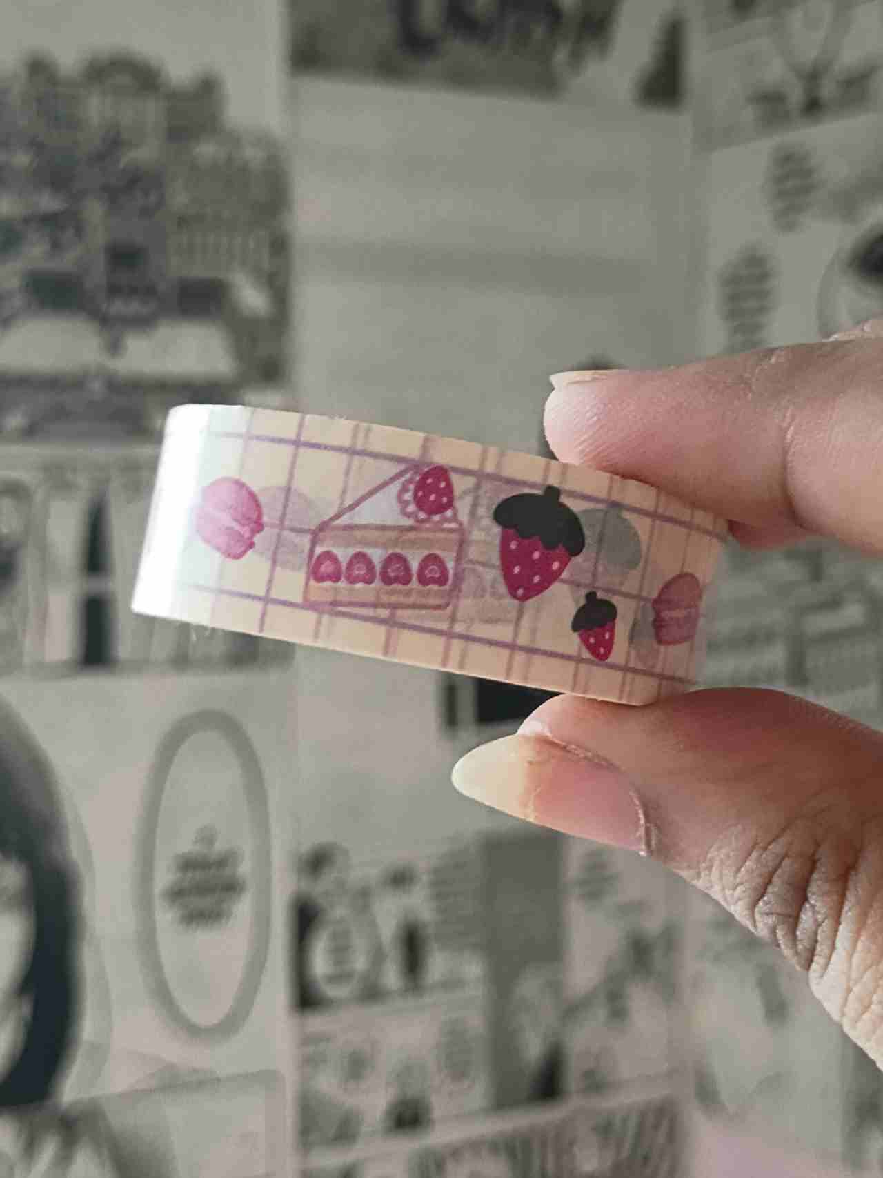 Hand holding a roll of Strawberry treats decorative tape with strawberry desserts pattern against a manga background