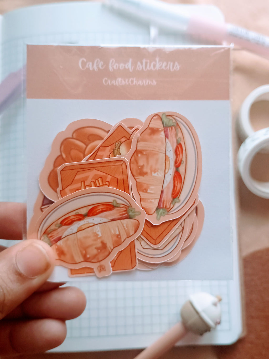 Pack of cafe food stickers with burger and fries, americano, latte, croissant sandwitch, egg sandwitch, onion ings, potato wedges and carbonara with garlic bread held by a hand 